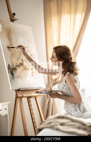 Beautiful female painter enjoying while painting in home art studio. Woman Artist Works on Abstract acrylic painting in the art studio. Stock Photo