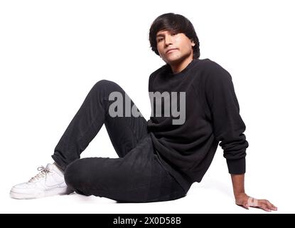 A man in a black sweatshirt and black pants is sitting on the floor. He is wearing white shoes Stock Photo