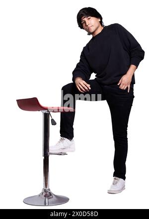 A man in a black sweatshirt is sitting on a red stool. He is wearing white sneakers and has his hands in his pockets Stock Photo