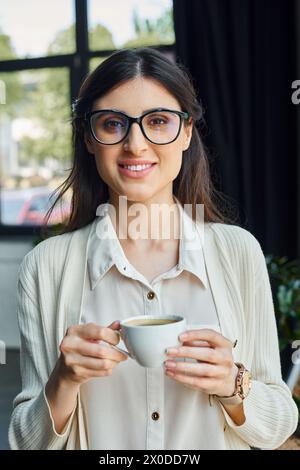 A businesswoman with glasses enjoys a coffee break in a modern office workspace. Stock Photo
