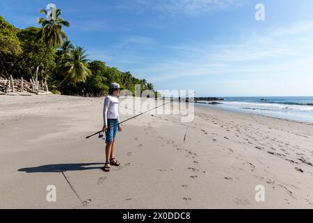 Kid, tourist, with a fishing rod in his hand exploring beach Playa Montezuma near Montezuma village on a beautiful summer sunny day, Costa rica Stock Photo