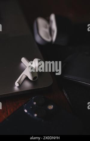 A pair of sleek, white, wireless earphones rest on a silver laptop with a black keyboard. The earphones are designed for comfort and style. Stock Photo