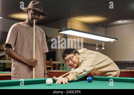 Portrait of two smiling friends playing pool together at billiards club with Asian man looking at camera copy space Stock Photo