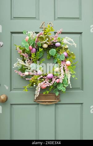 Kitsch plastic  Easter wreath with artificial pastel painted Easter eggs decoration foliage on a green front door in Wales Ceredigion UK KATHY DEWITT Stock Photo
