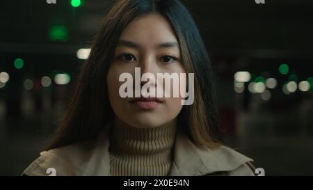 Close up portrait pensive serious Asian chinese ethnic woman young girl businesswoman female in dark parking city unhappy customer car owner client Stock Photo