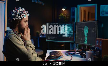 IT technician using EEG headset stupefied after mind upload virtual process is successful. Man astounded after achieving goal of transferring consciousness into computer cyberspace, camera B Stock Photo