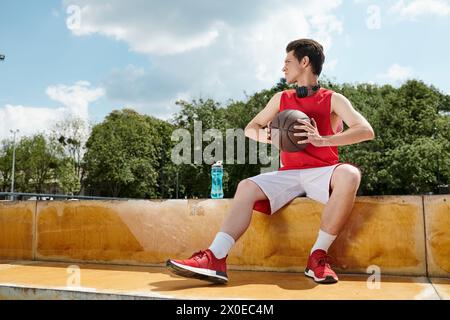 A young basketball player sitting on a ledge, skillfully holding a basketball. Stock Photo