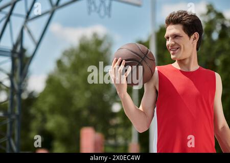 A young man in a fiery red shirt grips a basketball, preparing to shoot under the hot summer skies. Stock Photo