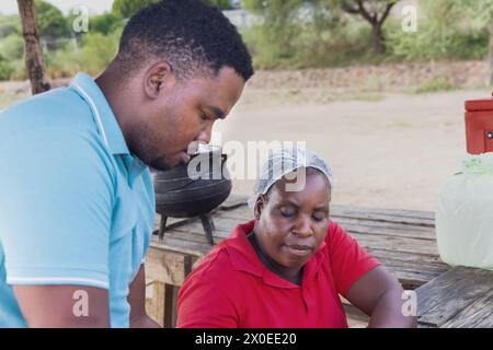 woman african street vendor selling cooked setswa food to a man client from a large pot on the side of the highway Stock Photo