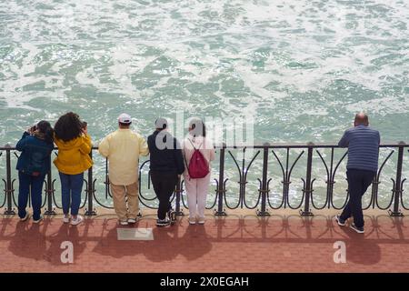 Tarragona, Spain - April 11, 2024: People of different ages in Tarragona observe the waves of the sea from a railing, creating a relaxing and contempl Stock Photo