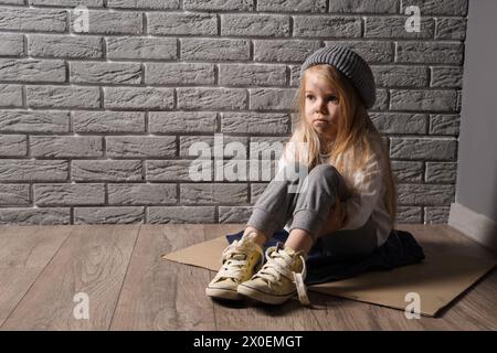 homeless little girl sitting on floor near grey brick wall Stock Photo