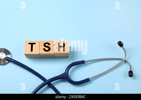 Endocrinology. Stethoscope and wooden cubes with thyroid hormones on light blue background. Space for text Stock Photo