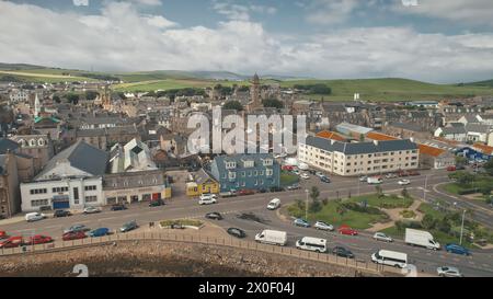 Pier town at sun shine over buildings roofs aerial. Traffic road at sea bay coast. Ships, vessel, yacht at harbor. Sunny urban highway with cars, buses, trucks. Campbeltown cityscape, Scotland, Europe Stock Photo