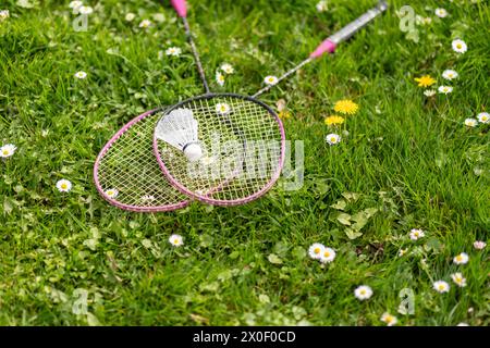 Two badminton rackets and a shuttlecock lie on the green grass. Outdoor recreation and fresh air. The sun's rays. Lawn for playing badminton. Stock Photo