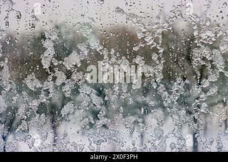 Drops of ice and rain on a window overlooking a winter snow-covered forest. Ice and water on the window close-up. Stock Photo