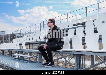 One young man sitting on empty football tribune on the street Stock Photo