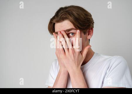 Young Man Covering His Face With His Hands Against a Neutral Background Stock Photo