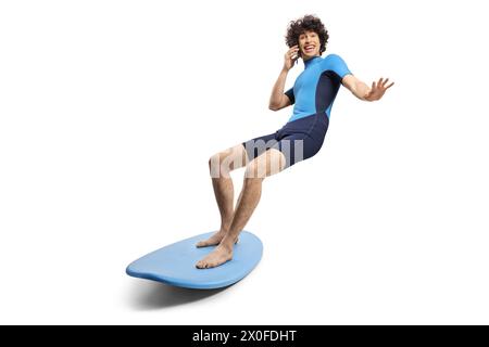 Young man in a wetsuit riding a surfboard and using a smartphone isolated on white background Stock Photo