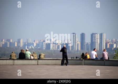 KYIV, UKRAINE - APRIL 11, 2024 - People sit on the ledge facing high rises on the left bank of the Dnipro River, Kyiv, capital of Ukraine. Stock Photo