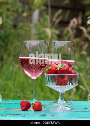 Two glasses of rose sparkling wine and strawberry on a  table. Romantic picnic outdoors. Close up photo of glass tableware. Summer drinks and food. Stock Photo