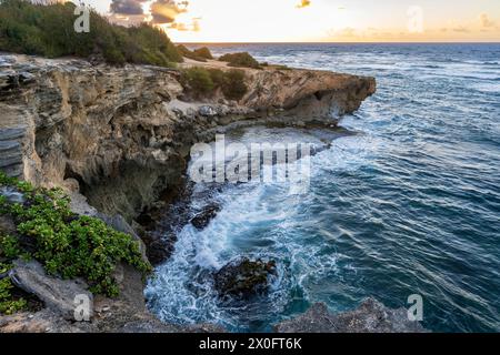 The sun slowly rises over jagged cliffs, meeting the rough turquoise waters of the Pacific Ocean along the Mahaulepu Heritage Trail in Koloa, Hawaii Stock Photo