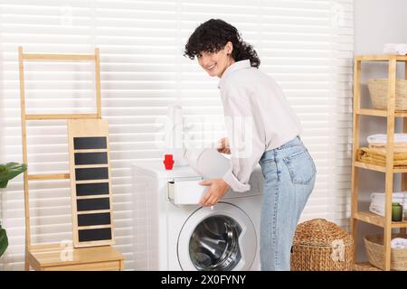 Woman pouring laundry detergent into washing machine indoors Stock Photo