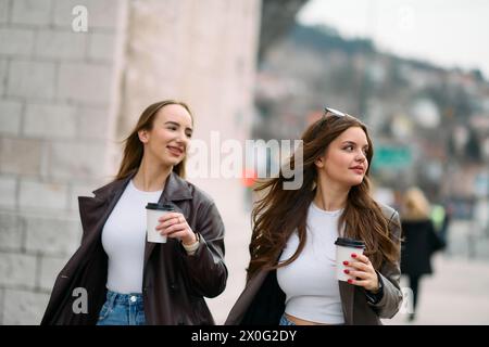 Two beautiful business women go to work while holding cups of coffee in their hands Stock Photo