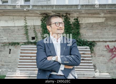 Businessman Sitting on Bench with Cityscape in the Background Stock Photo