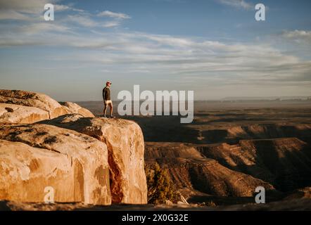 Man in shorts stands at edge of cliff overlooking San Jaun River, Utah Stock Photo