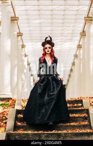 Witchy girl in black dress wearing horns walking down stairs Stock Photo