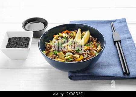 Stir-fry. Delicious cooked noodles with chicken and vegetables in bowl served on white wooden table Stock Photo