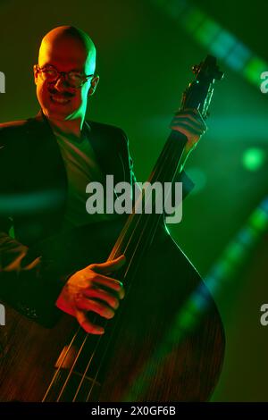 Contemporary double bass player in silhouette in red-green neon light against gradient studio background. Stock Photo