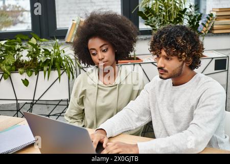 A diverse group of students working on a laptop together at a table in a modern coworking space. Stock Photo