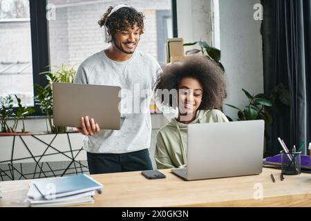 A multicultural man and woman focused on laptops, collaborating in a modern office coworking space. Stock Photo