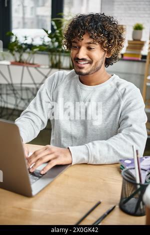 A man from a diverse group sits at a table, absorbed in his laptop screen in a modern coworking space. Stock Photo