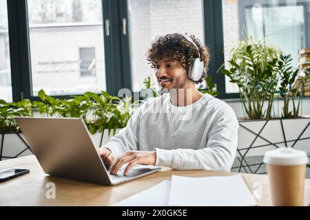 A man of diverse background sits focused in front of a laptop in a modern coworking space. Stock Photo