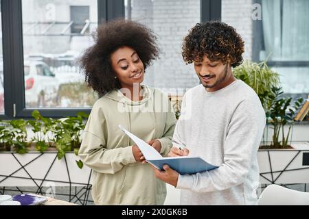 A man and a woman of different cultures focus intently on a piece of paper, engaged in a shared learning experience. Stock Photo