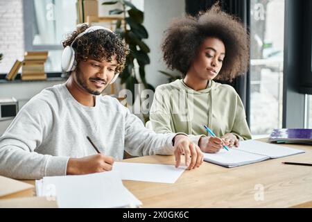 A man and woman of different ethnicities sit at a table, focused on paperwork and collaborating in a modern coworking space. Stock Photo