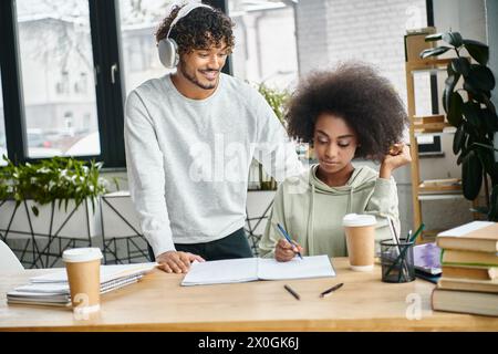 A multicultural man and woman engage in productive discussion at a table in a modern office space, surrounded by digital devices. Stock Photo