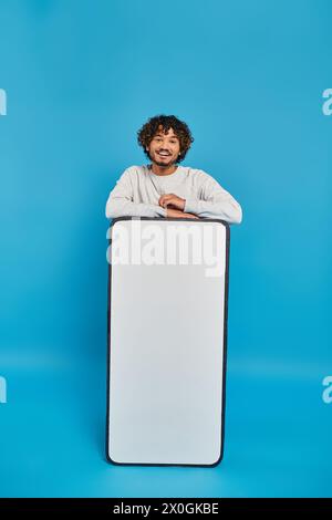 A man stands hidden behind a large white object in a studio setting on a blue background. Stock Photo