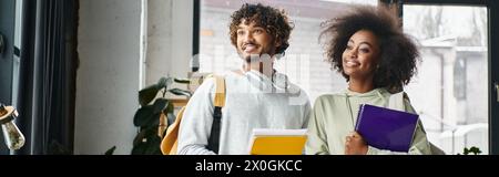 A man and a woman of different ethnicities stand close together in front of a window, creating a heartwarming scene of diversity and unity. Stock Photo