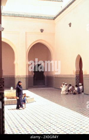 A woman with a child walks past a group of men sitting on the ground in the courtyard of the Mulai Ismail burial mosque in Meknes. [automated translation] Stock Photo