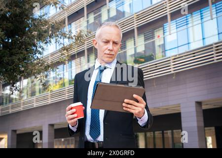 Portrait of smiling businessman using an app on hisdigital tablet and standing  Stock Photo