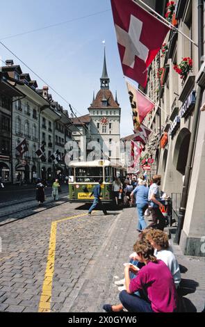 A group of women squatting on the tram waiting for the pavement on Marktgasse in Bern with the cage tower in the background. [automated translation] Stock Photo