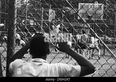 A boy is looking at a basketball game through a fence in Manhattan in New York City. Stock Photo