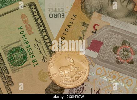 one ounce original 24 carat South African Kruger rand gold coin vs with several common fiat paper currencies; dollar, euro, riyal aud; anti inflation Stock Photo