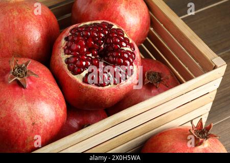 Ripe pomegranates in wooden crate on table, closeup Stock Photo