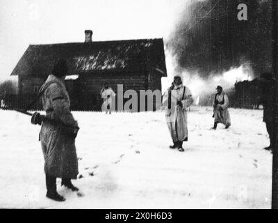Soldiers in winter camouflage leave a burning village after fighting on the Eastern Front. The picture was taken in the rear of the Eastern Front, presumably in connection with battles with partisans. The picture was taken by a member of the Raffahrgrenadier Regiment 2 / Rahdfahrsicherungsregiment 2, in the northern section of the Eastern Front. [automated translation] Stock Photo