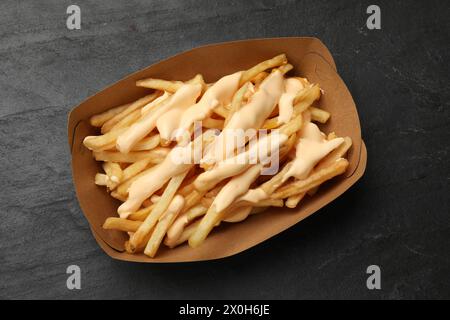 Tasty potato fries and cheese sauce in paper container on black table, top view Stock Photo