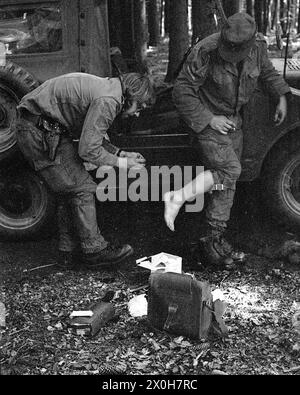 During a military exercise of the II Corps of the German Armed Forces in the Swabian Alb, a medic treats another soldier in uniform. The latter has blistered his feet. Medical equipment lies on the ground. Parts of a truck can be seen in the background. [automated translation] Stock Photo